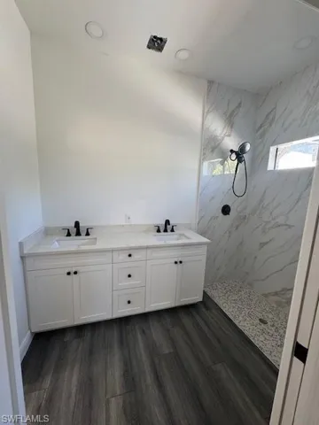 Bathroom with double vanity, a marble finish shower, and dark wood finished floors