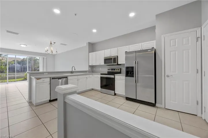 Kitchen featuring appliances with stainless steel finishes, white cabinetry, light tile patterned floors, a peninsula, and decorative light fixtures