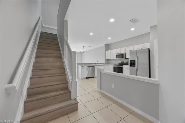 Kitchen featuring stainless steel appliances, white cabinets, a peninsula, light tile patterned flooring, and light countertops