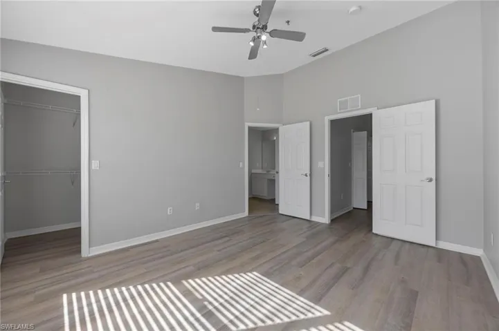 Unfurnished bedroom featuring a spacious closet, light wood-style flooring, a high ceiling, and a ceiling fan