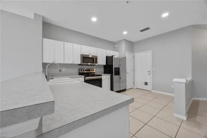 Kitchen featuring white cabinets, appliances with stainless steel finishes, light countertops, light tile patterned floors, and recessed lighting