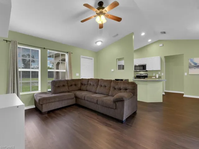 Living room with ceiling fan, vaulted ceiling, and dark wood-type flooring
