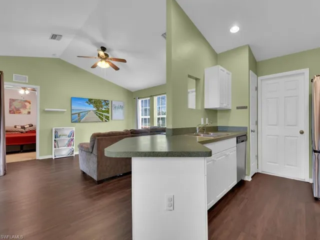 Kitchen featuring kitchen peninsula, vaulted ceiling, dark wood-type flooring, sink, and white cabinetry
