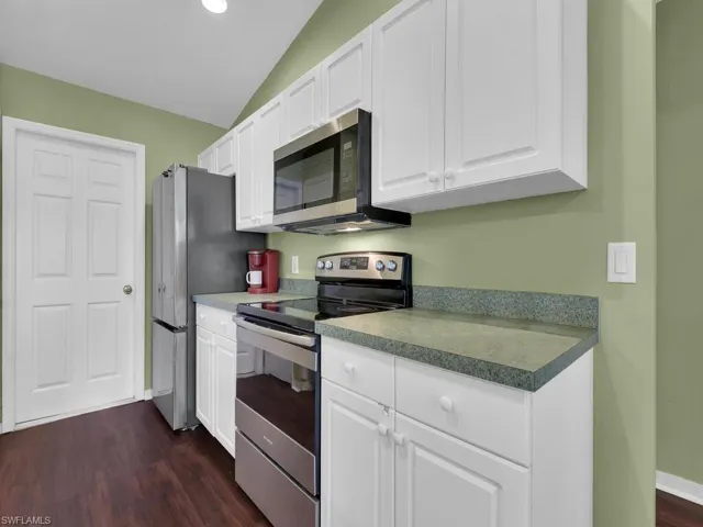 Kitchen with dark hardwood / wood-style floors, stainless steel appliances, white cabinets, and lofted ceiling