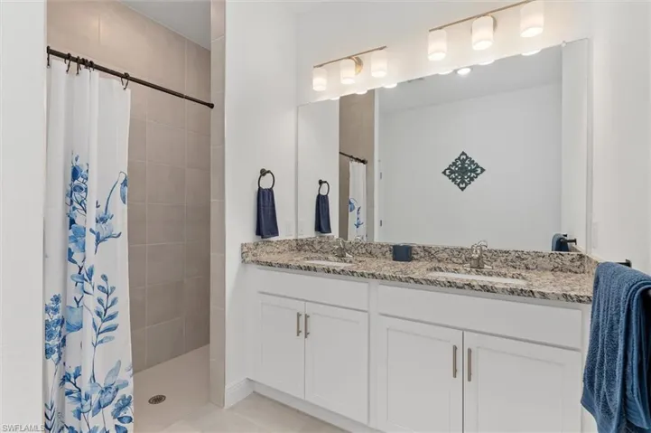 Full bathroom featuring double vanity and tiled shower