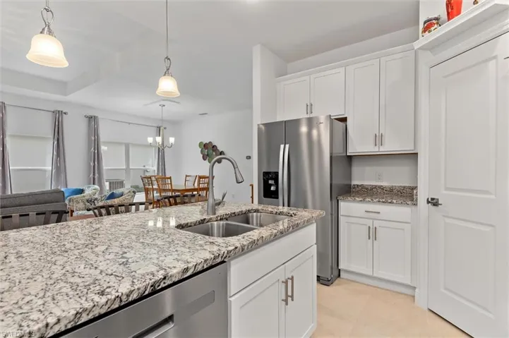Kitchen featuring white cabinetry, stainless steel appliances, light stone counters, hanging lights, and light tile patterned floors