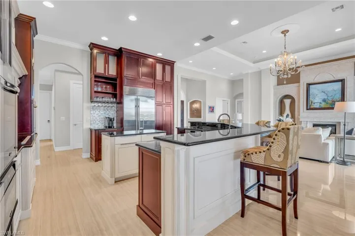 Kitchen featuring stainless steel built in fridge, tasteful backsplash, hanging light fixtures, an inviting chandelier, and a kitchen island with sink