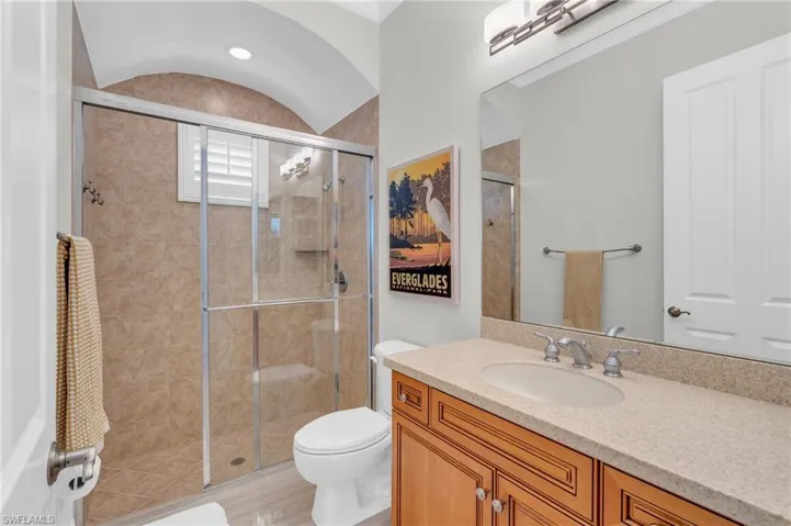 Bathroom featuring toilet, vanity, vaulted ceiling, and a shower with door