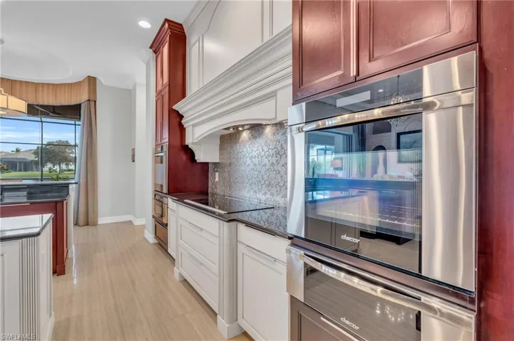 Kitchen with custom exhaust hood, black electric stovetop, tasteful backsplash, and stainless steel double oven