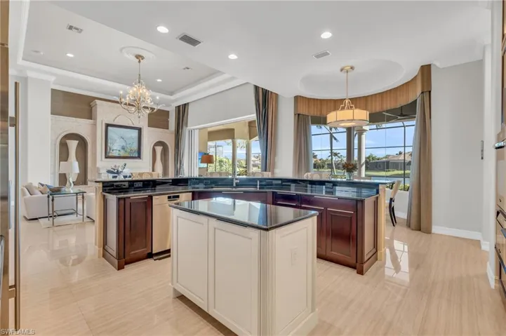 Kitchen with a raised ceiling, a center island, pendant lighting, stainless steel dishwasher, and a chandelier
