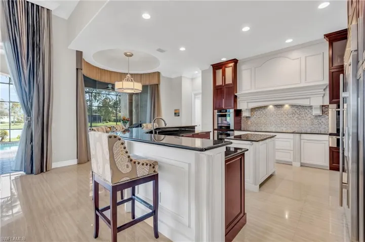 Kitchen featuring appliances with stainless steel finishes, sink, backsplash, decorative light fixtures, and a center island with sink