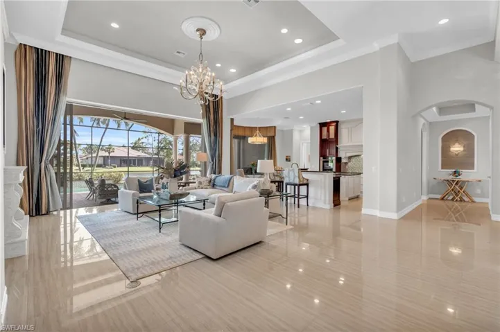 Tiled living room with crown molding, a tray ceiling, and an inviting chandelier