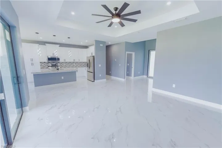 Kitchen with decorative light fixtures, stainless steel appliances, a tray ceiling, a center island with sink, and light tile patterned floors