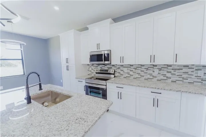 Kitchen with stainless steel appliances, sink, decorative backsplash, light stone countertops, and white cabinetry