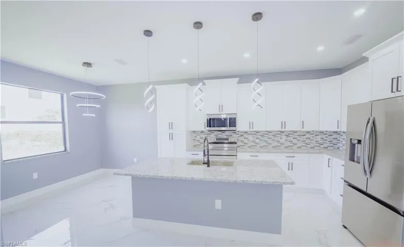 Kitchen with appliances with stainless steel finishes, light stone counters, hanging light fixtures, a kitchen island with sink, and light tile patterned flooring