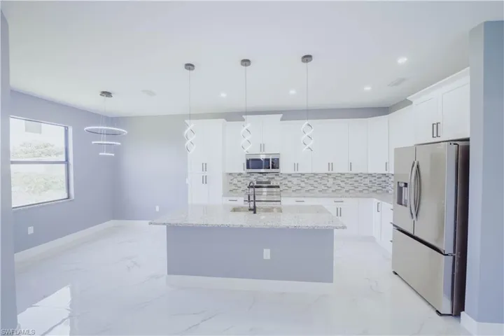 Kitchen with light tile patterned flooring, backsplash, an island with sink, appliances with stainless steel finishes, and decorative light fixtures