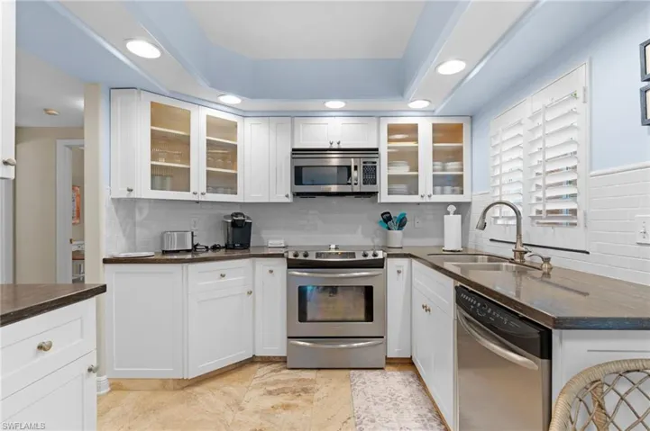 Kitchen with stainless steel appliances, white cabinets, sink, and tasteful backsplash