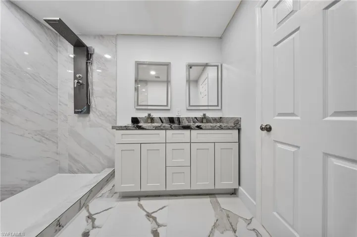 Modern bathroom featuring a spacious walk-in shower with a rainfall showerhead, dual vanity with white shaker-style cabinetry, dark speckled countertops, and framed mirrors