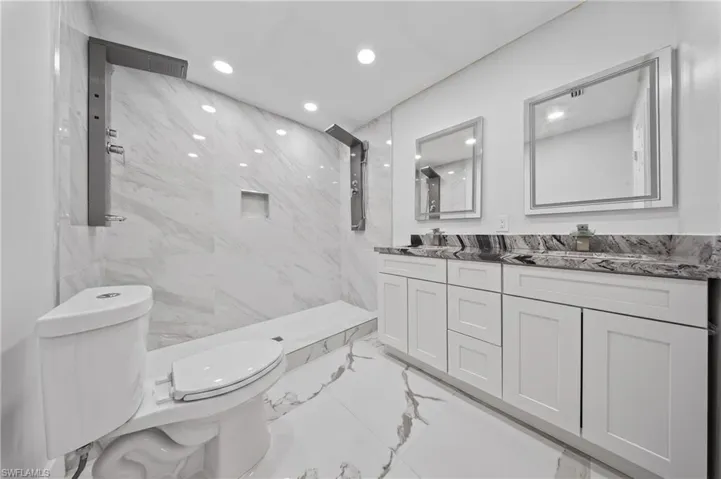 Contemporary bathroom featuring a spacious shower with multiple showerheads, a tiled bench, and a recessed niche