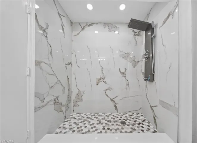 Shower featuring large format white and gray veined wall tiles, a multi-function shower panel with overhead rain shower, recessed lighting, and a mosaic tiled shower bench