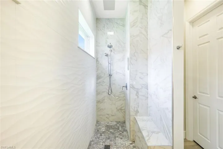 Walk-in shower with textured wall tile, pebble-tiled floor, built-in bench, dual shower heads, and an upper window