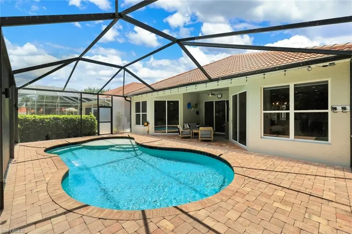 Screened-in outdoor living space featuring a freeform swimming pool with steps, a paver patio, and exterior access to the interior