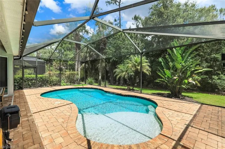 Screened-in outdoor living space featuring a freeform swimming pool with a shallow entry and surrounding brick paver deck