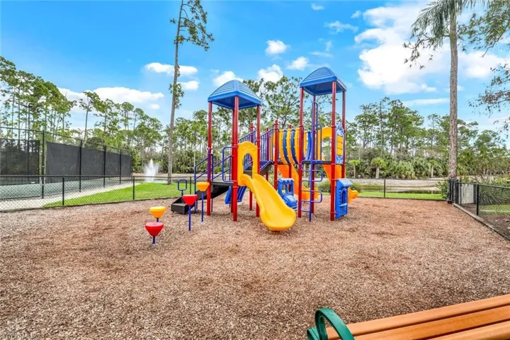 Community playground featuring a colorful multi-structure play area, wood chip surfacing, and a perimeter fence