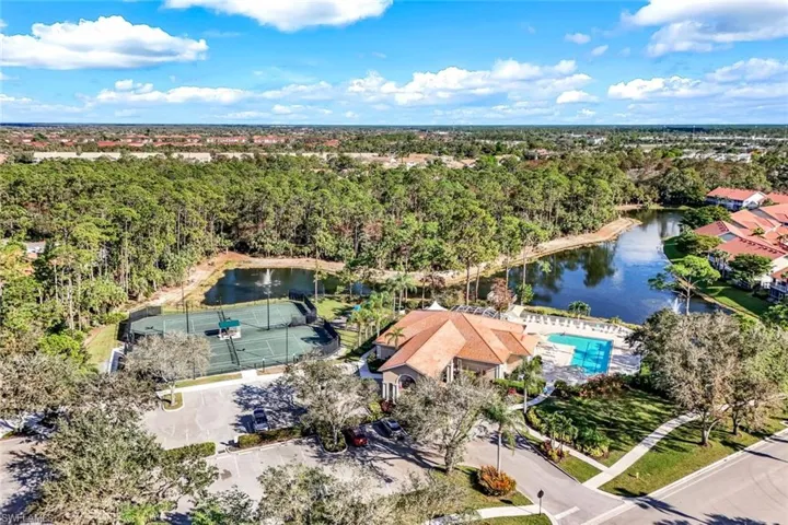 Aerial view showcasing a community building with a tile roof, an outdoor swimming pool with surrounding lounge chairs, and two tennis courts