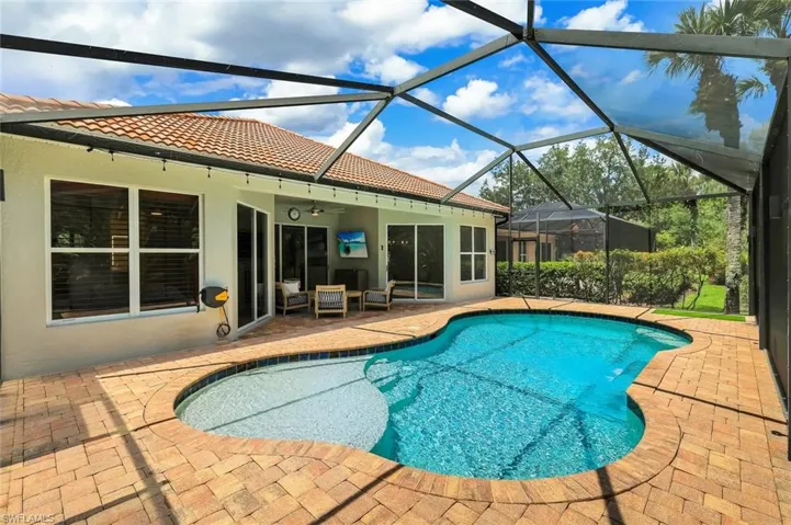Screened-in outdoor pool and patio area featuring a freeform pool with integrated spa, terracotta tile roof, and a paved patio surround