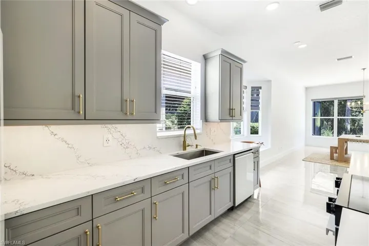 Kitchen featuring light grey shaker cabinetry, brushed brass hardware, quartz countertops, and a stainless steel sink with a gold-finish faucet