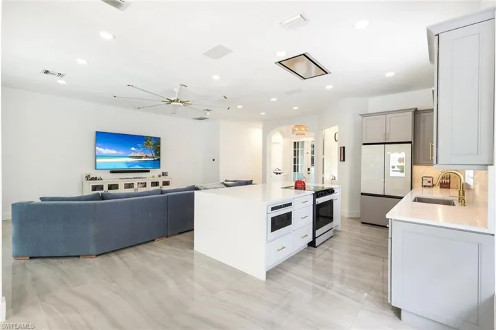 Open-concept living space featuring a central kitchen island with built-in microwave, light gray cabinetry, integrated stainless steel appliances, and wood-finish flooring