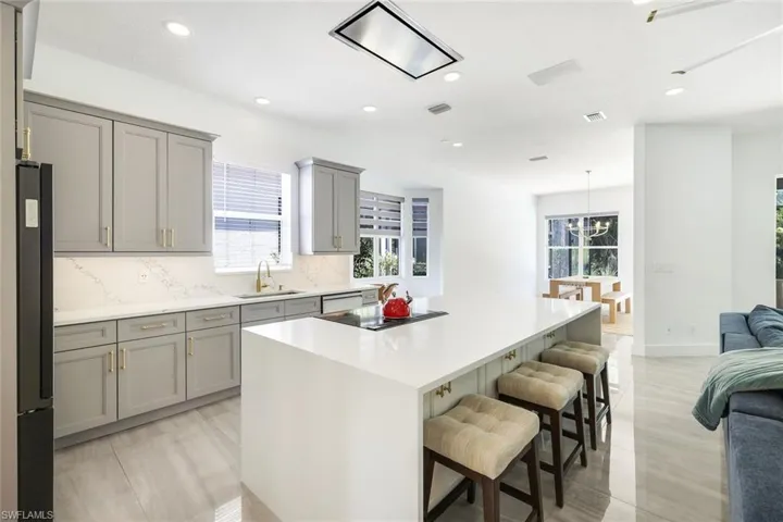 Contemporary kitchen featuring a large center island with integrated cooktop, grey shaker-style cabinetry, white countertops and backsplash, and recessed lighting