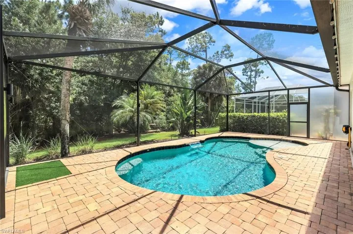 Screened pool area featuring a freeform swimming pool, extensive paver decking, lush perimeter landscaping, and a privacy screen enclosure