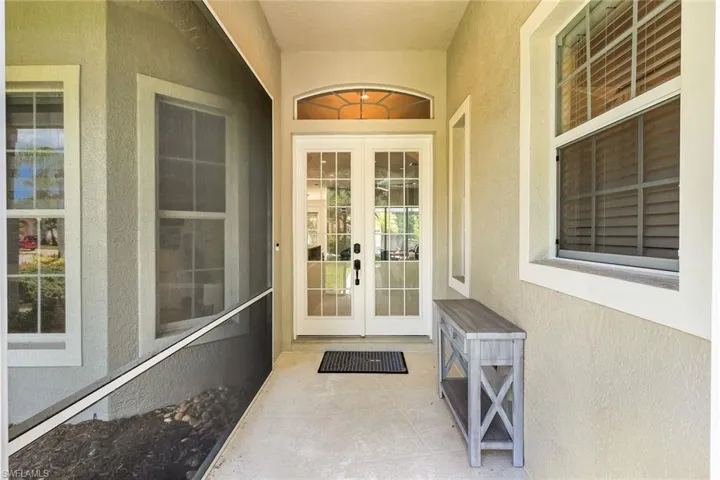 Entryway featuring double French doors with transom window, screened enclosure, textured stucco exterior, and multi-pane windows with louvered blinds