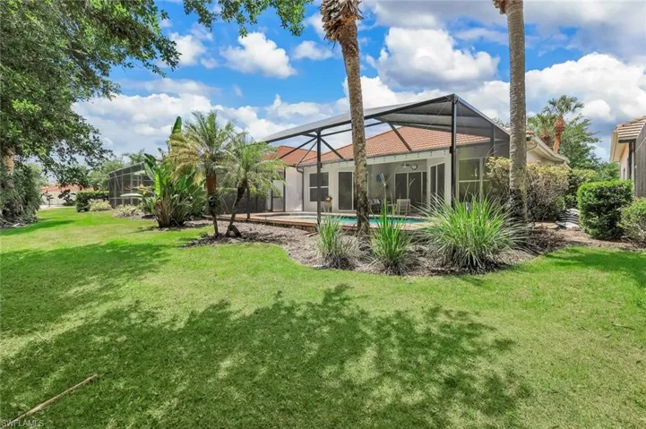 Expansive backyard featuring a green lawn, mature trees, and tropical landscaping