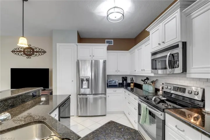 Kitchen with appliances with stainless steel finishes, backsplash, white cabinetry, and dark stone counters