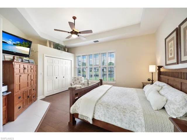 Bedroom featuring a double closet, hardwood flooring, a tray ceiling, plantation shutters