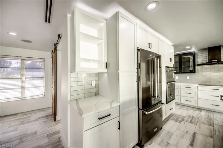 Kitchen with open floor plan, a barn door, light countertops, a center island with sink, and recessed lighting