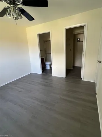 Unfurnished bedroom with dark wood-style flooring, ensuite bathroom, and ceiling fan