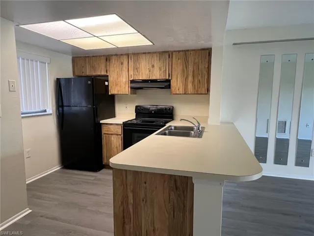 Kitchen with black appliances, light countertops, brown cabinetry, a peninsula, and wood finished floors
