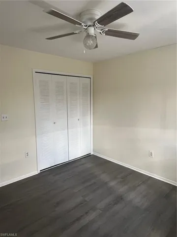 Unfurnished bedroom featuring dark wood-style floors, a closet, and a ceiling fan