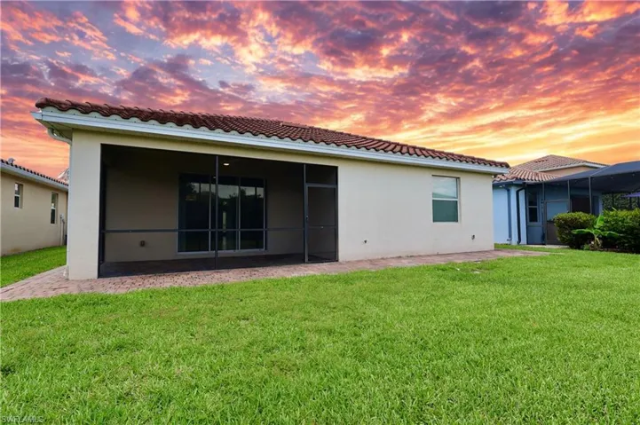 Back of property at dusk with stucco siding, a yard, and a tiled roof
