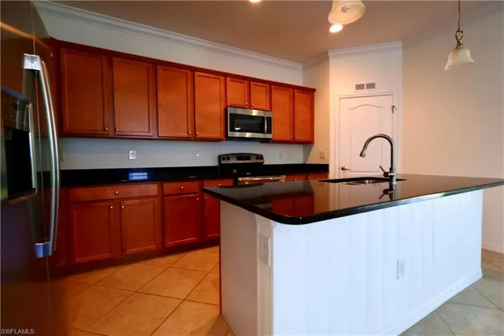 Kitchen featuring appliances with stainless steel finishes, ornamental molding, dark countertops, light tile patterned floors, and a kitchen island with sink