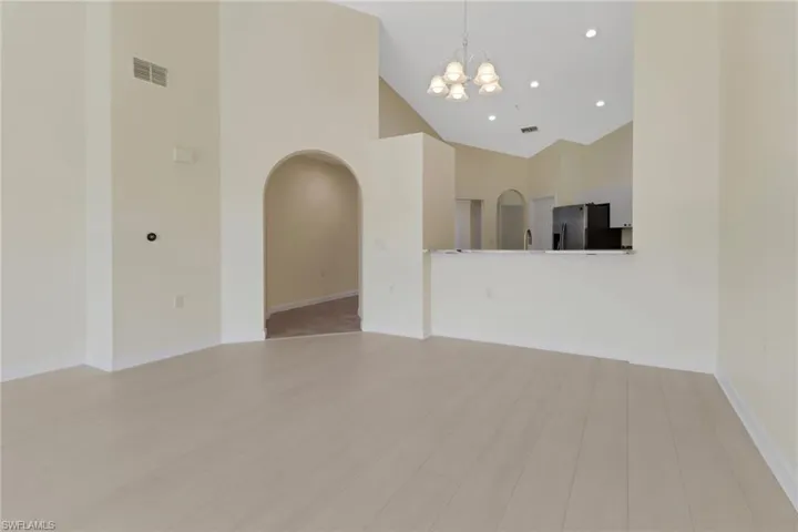 Unfurnished living room featuring high vaulted ceiling, light hardwood / wood-style flooring, and a notable chandelier