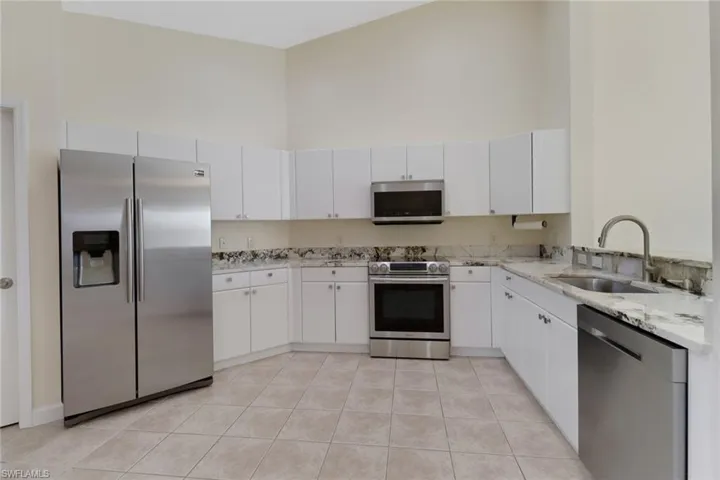 Kitchen featuring stainless steel appliances, white cabinetry, sink, and a towering ceiling
