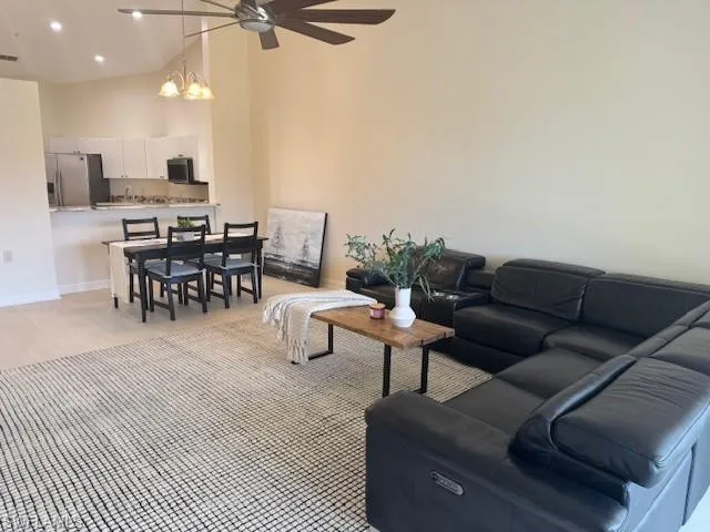 Living room featuring recessed lighting, high vaulted ceiling, baseboards, and ceiling fan with notable chandelier