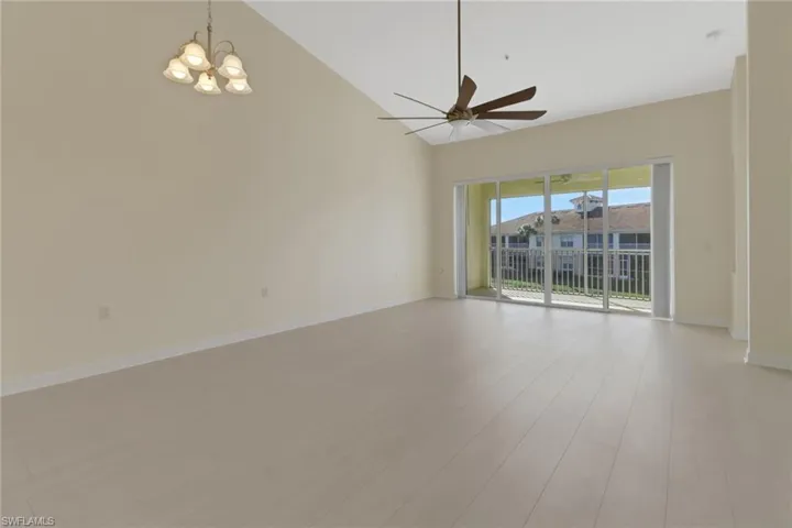 Spare room featuring high vaulted ceiling, ceiling fan with notable chandelier, and light wood-type flooring