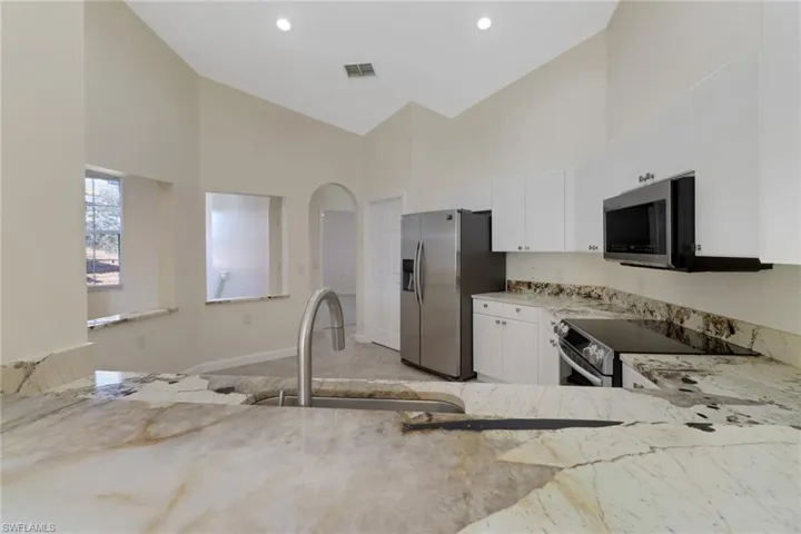 Kitchen with white cabinetry, sink, stainless steel appliances, and high vaulted ceiling