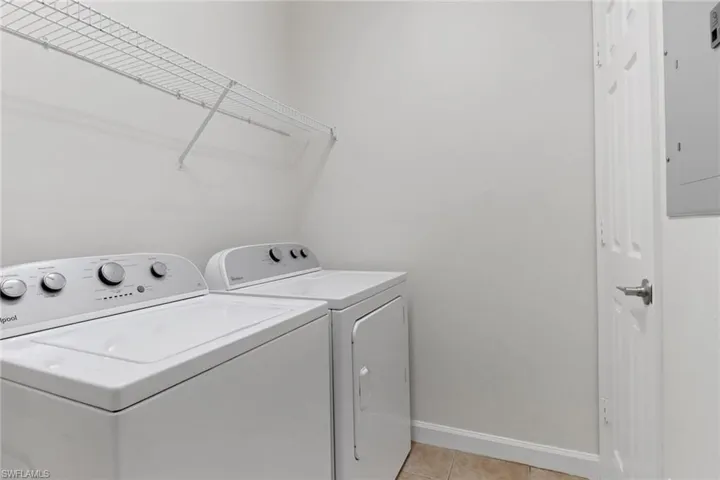 Clothes washing area featuring separate washer and dryer, light tile patterned floors, and electric panel